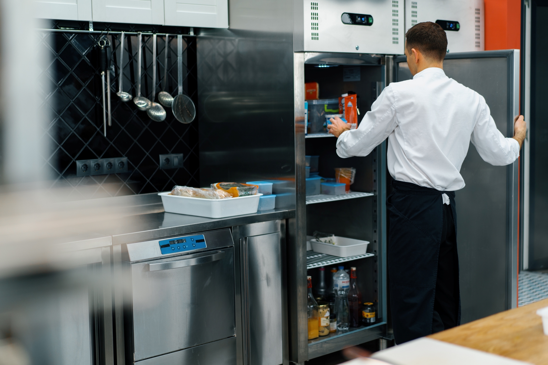 Professional kitchen chef looks into the fridge and chooses ingredients for cooking food concept