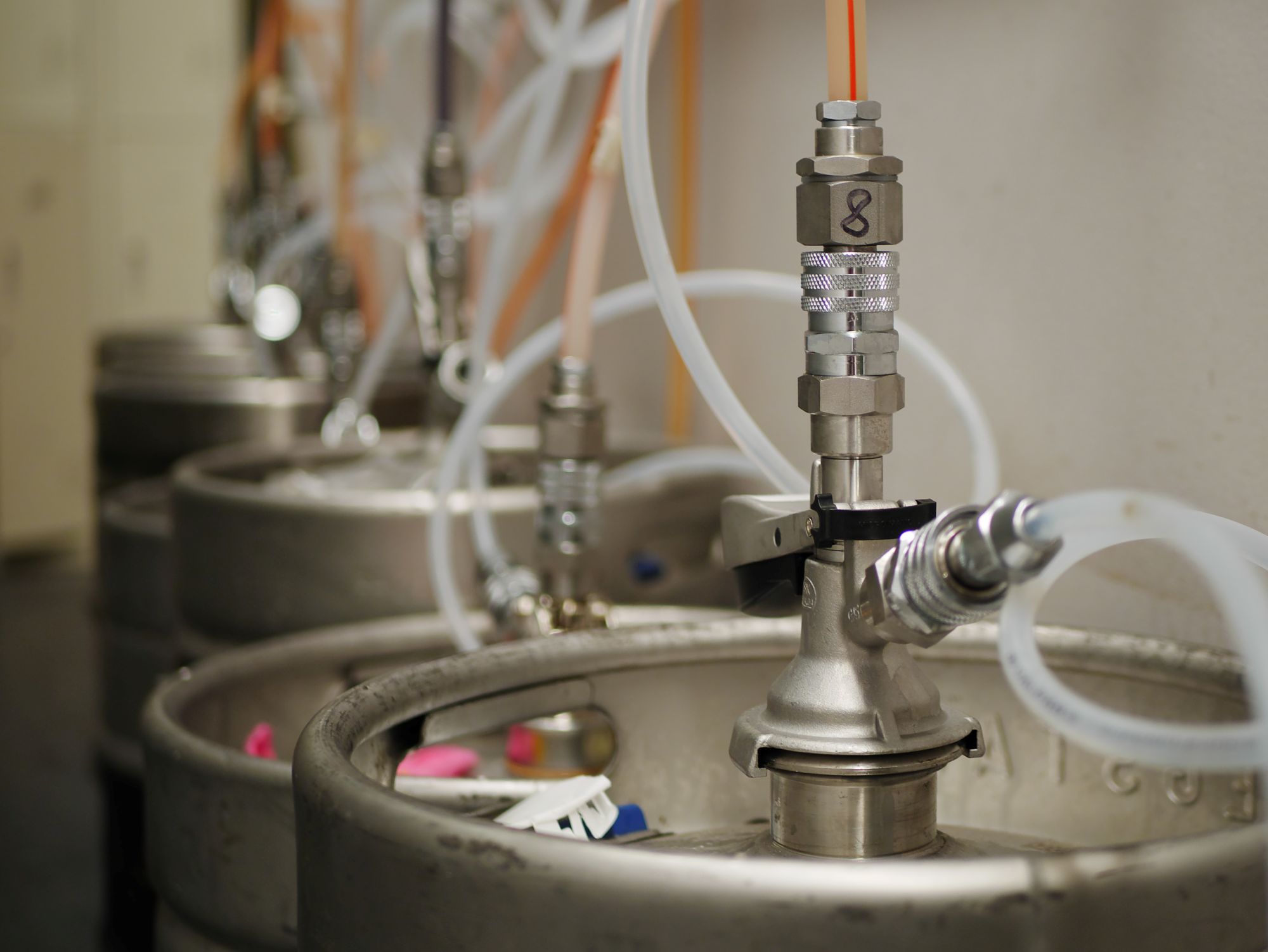Row of beer kegs connected by hoses and taps in a storage area, conveying an industrial and functional atmosphere with a focus on beverage dispensing.